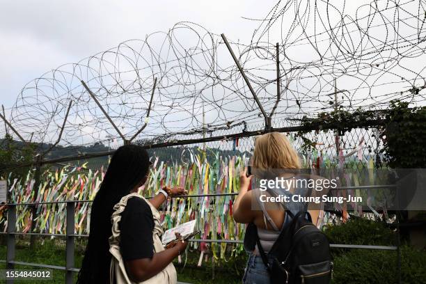 Tourists take pictures of prayer ribbons wishing for reunification of the two Koreas on the wire fence at the Imjingak Pavilion, near the...