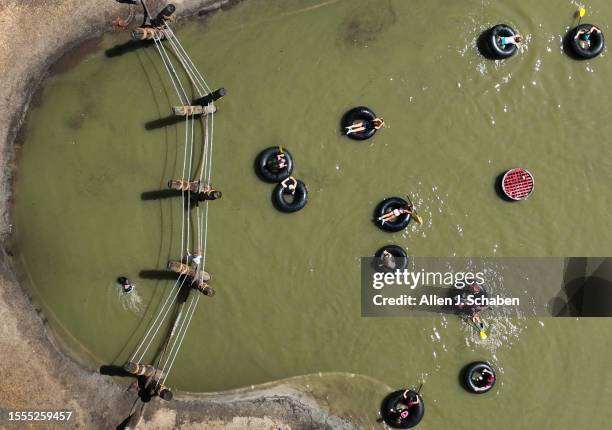 Huntington Beach, CA Kids play on a rope bridge and paddle inner tubes on a small pond at Adventure Playground amidst a hot day in Huntington Central...