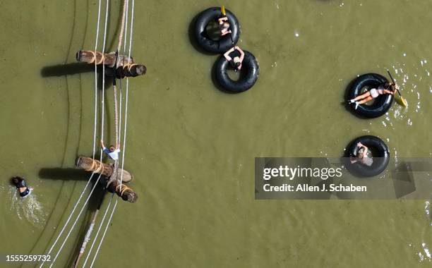 Huntington Beach, CA Kids play on a rope bridge and paddle inner tubes on a small pond at Adventure Playground amidst a hot day in Huntington Central...