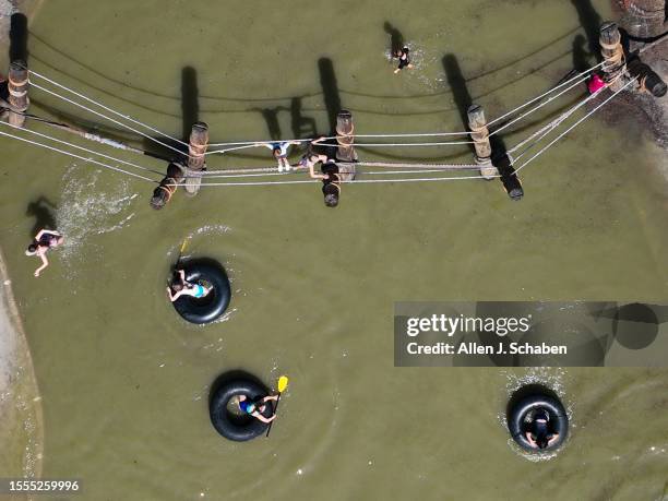 Huntington Beach, CA Kids play on a rope bridge and paddle inner tubes on a small pond at Adventure Playground amidst a hot day in Huntington Central...