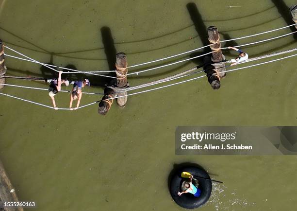 Huntington Beach, CA Kids play on a rope bridge and paddle inner tubes on a small pond at Adventure Playground amidst a hot day in Huntington Central...