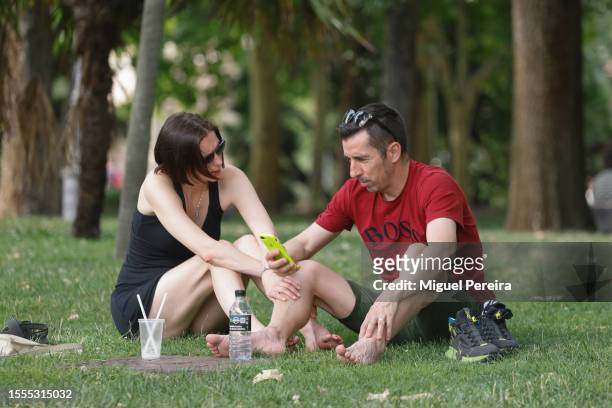 Man and a woman sit on the grass under the trees in a park on July 18, 2023 in Madrid, Spain. An area of high pressure, named Cerberus after the...