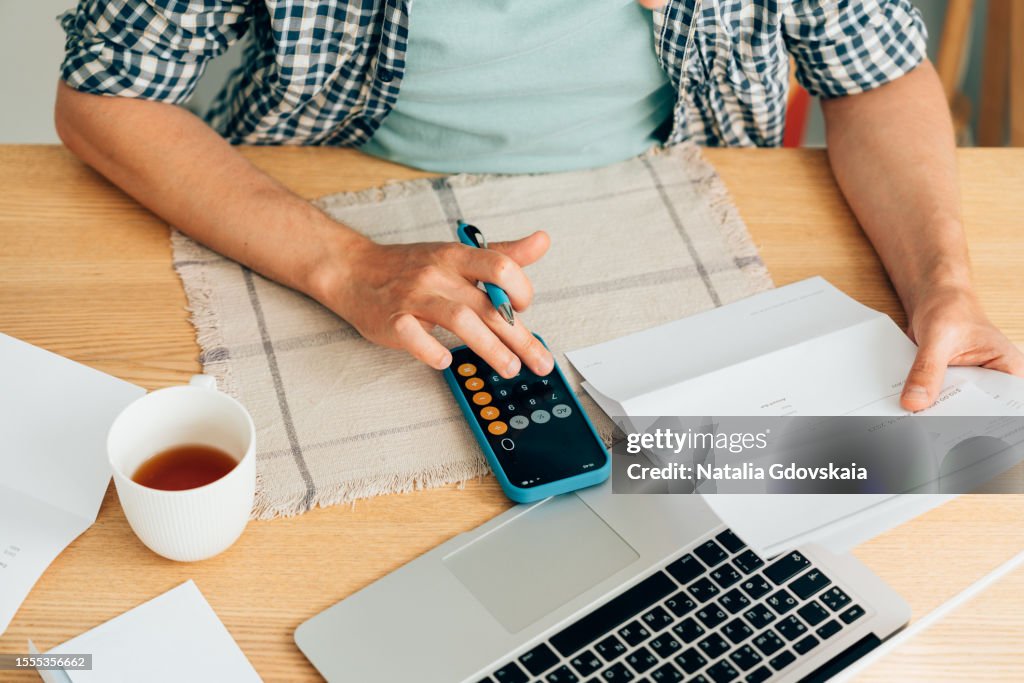 Man using calculator, analyzing financial data. Focused on work and working on budget or expense report. Man sitting at table in well-lit office.