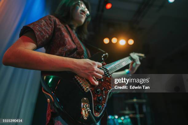 close up low angle young asian chinese guitarist plucking guitar at live band performance on stage - electronic music production stock pictures, royalty-free photos & images