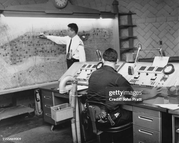 Police officer sits at a console as another inspects a map with the location of patrol cars, in the radio room at police headquarters in New York...