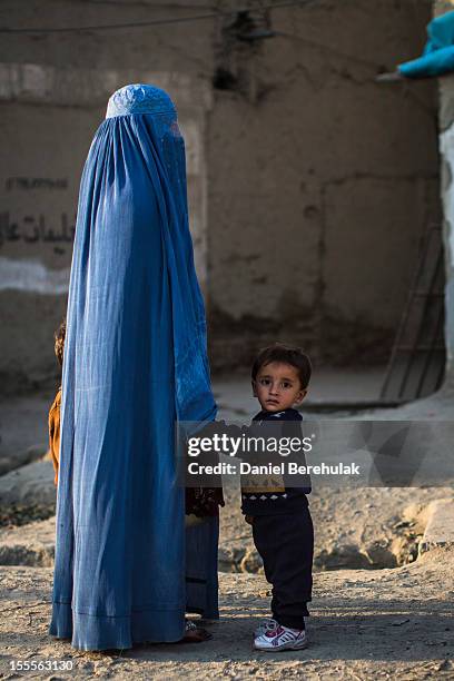 Young Afghan boy looks on as his hand is held roadside by a woman wearing a burqa on November 5, 2012 in Kabul, Afghanistan.