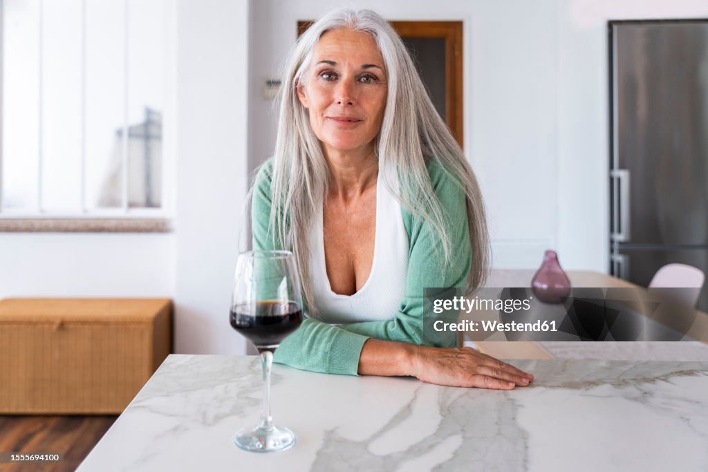 Smiling woman with glass of wine leaning on kitchen island