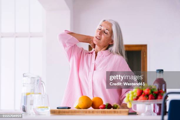 mature woman with gray hair stretching neck at home - neckache stock pictures, royalty-free photos & images