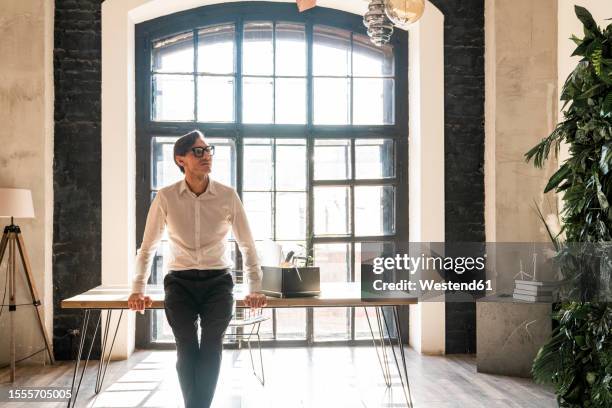 thoughtful mature businessman leaning on desk in office - cambio de oficina fotografías e imágenes de stock