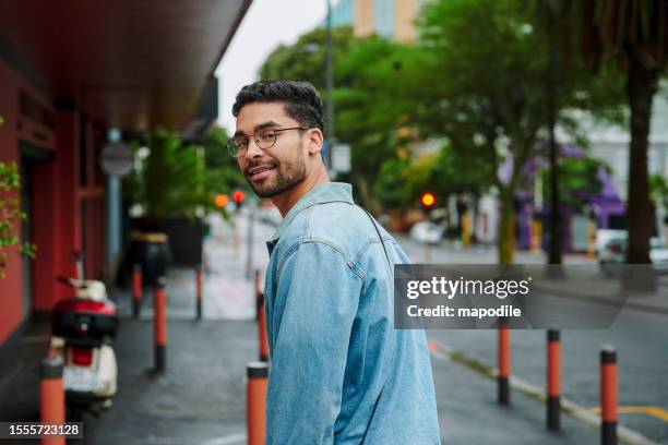 smiling young man looking over his shoulder while walking in the city - looking over shoulder stock pictures, royalty-free photos & images