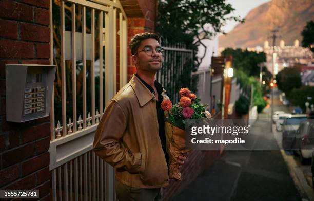 lächelnder junger mann wartet draußen mit blumen auf sein date - dating stock-fotos und bilder