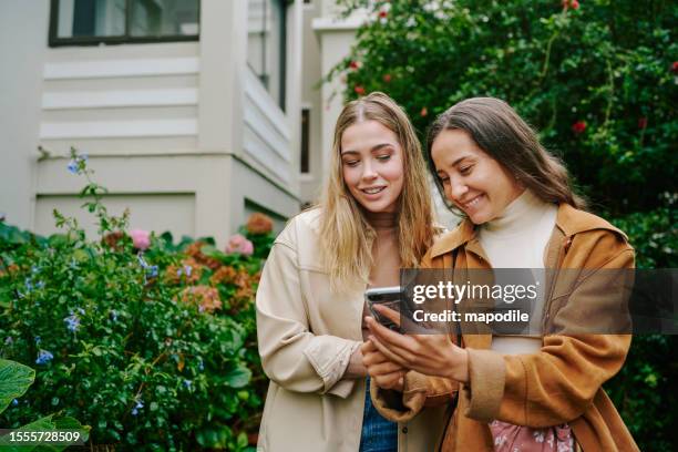 smiling young female friends swiping through a dating app outside - dating app stock pictures, royalty-free photos & images