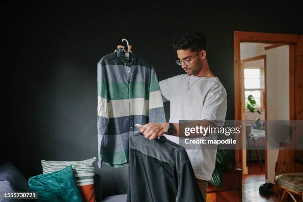 young man trying to choose a shirt to wear for a date - aankleden stockfoto's en -beelden