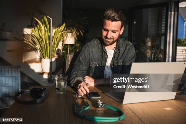 smiling freelancer using smart phone at desk - doctor using smartphone stock-fotos und bilder