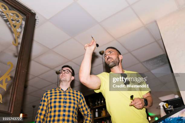 man aiming dart on target standing next to friend at bar - pub darts stock pictures, royalty-free photos & images