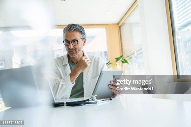 mature man in lab coat using tablet pc in clinic - doctor lab coat stock-fotos und bilder