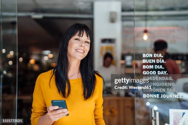 happy mature woman standing with mobile phone in doorway - multilingual stock pictures, royalty-free photos & images