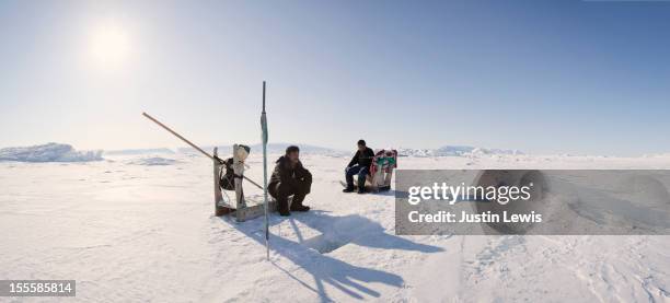 two inuit man rest while digging fish hole in ice - inuit foto e immagini stock