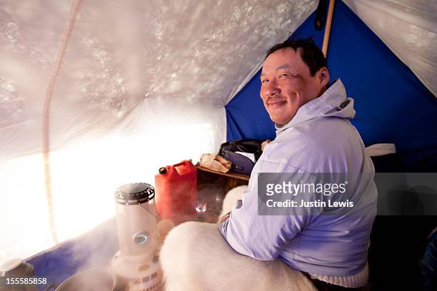 inuit man smiles inside tent while camped on ice - inuit people stock-fotos und bilder
