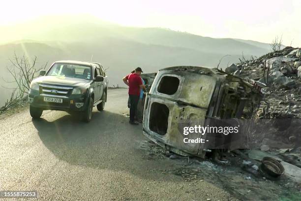 This image grab taken from AFPTV video footage shows people inspecting burnt-out vehicles on the side of a mountain road in the aftermath of...