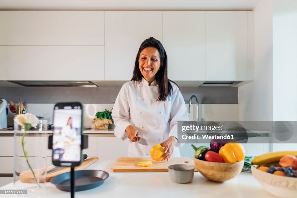 Happy chef cutting vegetable and vlogging through smart phone at home