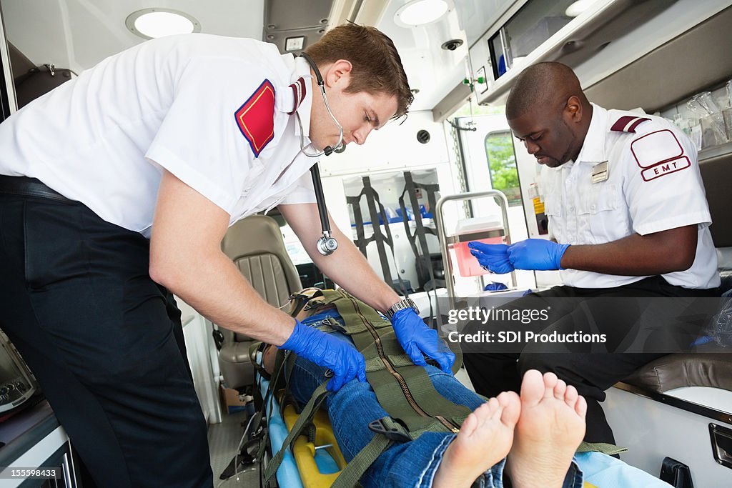 Medics strapping patient into ambulance stretcher