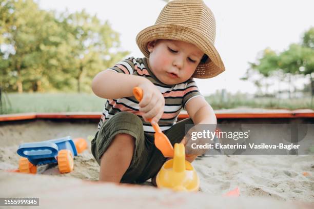 child in a hat playing in the sandbox - zandbak stockfoto's en -beelden