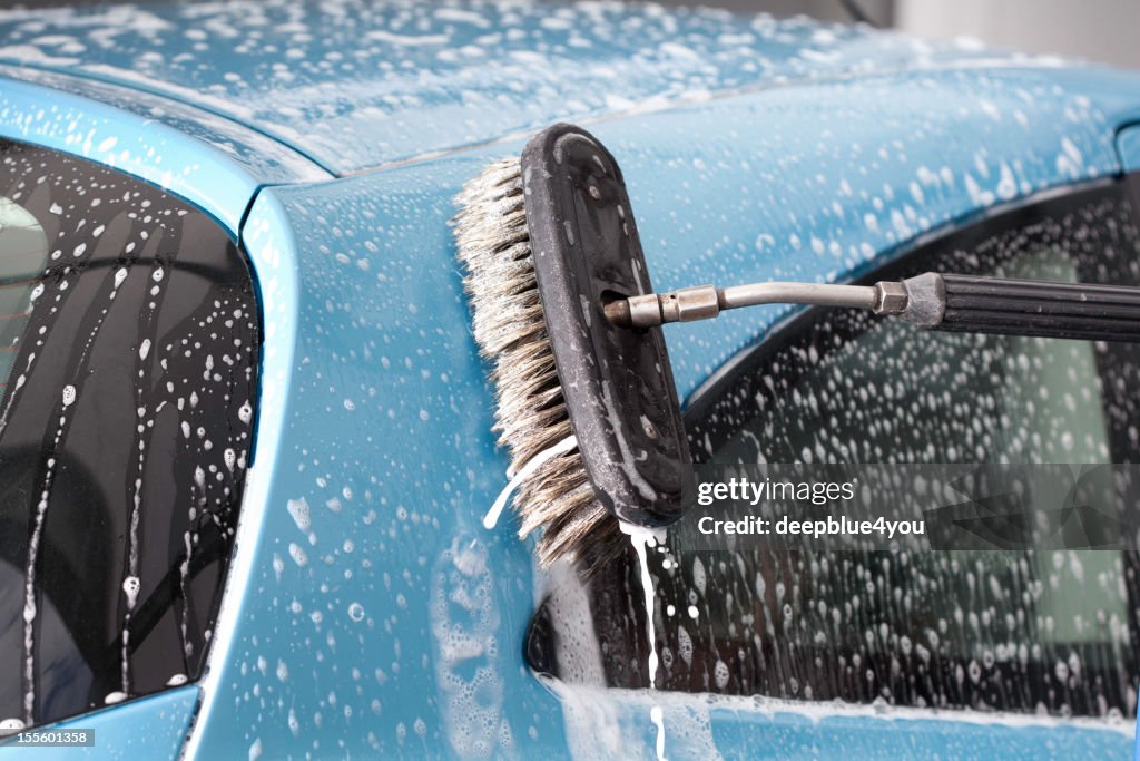 Brush is washing a blue car with foam