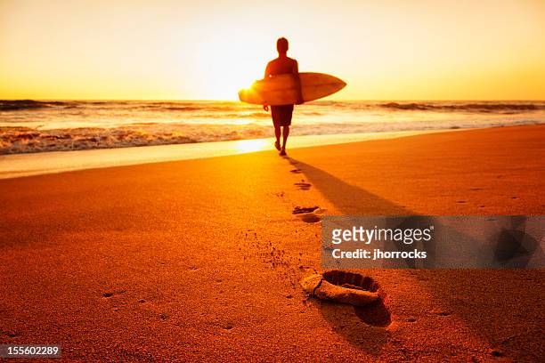 surfer bei sonnenuntergang - beach hold surfboard stock-fotos und bilder