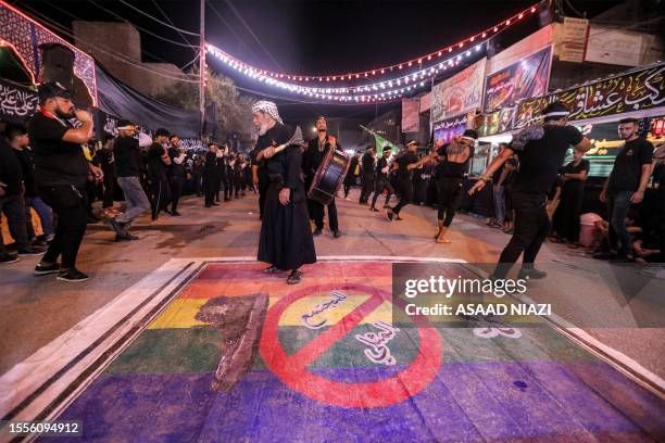 Shiite Muslim devotees self-flagellate over an unfurled banner on the ground depicting the Pride rainbow flag defaced with a boot and the Arabic...