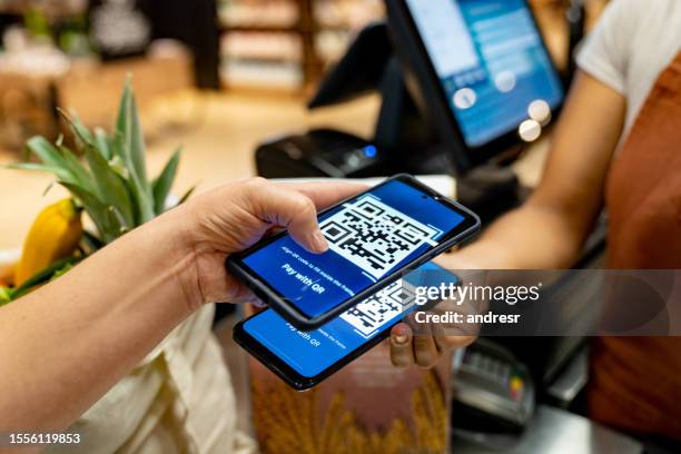 woman at the supermarket scanning a code to make a mobile payment - qr code stockfoto's en -beelden