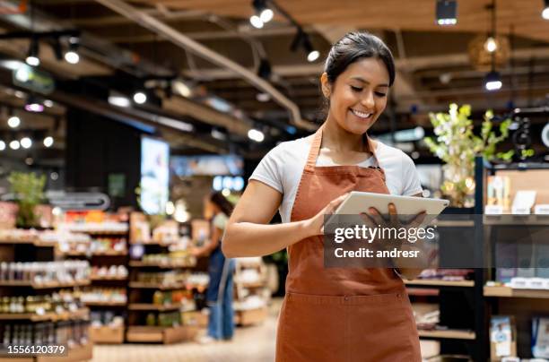 retail clerk using a tablet while working at the supermarket - latijns amerikaanse etniciteiten stockfoto's en -beelden