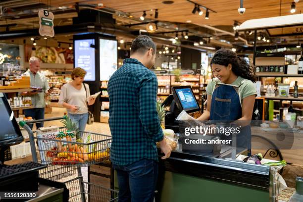 glückliche kassiererin, die im supermarkt arbeitet und produkte registriert - markt verkaufsstätte stock-fotos und bilder