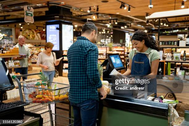 happy cashier working at the supermarket registering products - supermarket register stockfoto's en -beelden