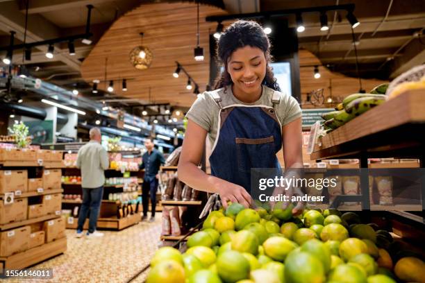 frau, die in einem supermarkt arbeitet und den obst- und gemüsegang auffüllt - verkäuferin stock-fotos und bilder