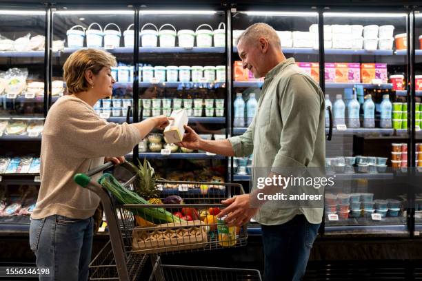 pareja de compras en el supermercado y señalando la fecha de caducidad de un poco de leche - fechas de caducidad fotografías e imágenes de stock