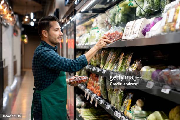 retail clerk working at a supermarket restocking the produce aisle - retail assistant stock pictures, royalty-free photos & images