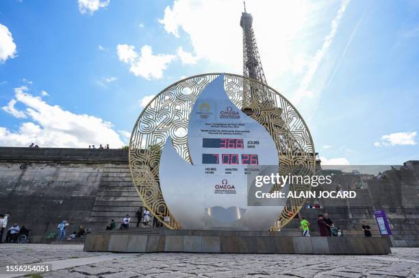 Pedestrians walk past a board displaying the countdown to the start of the Paris 2024 Olympic Games in front of the Eiffel Tower in Paris, on July...