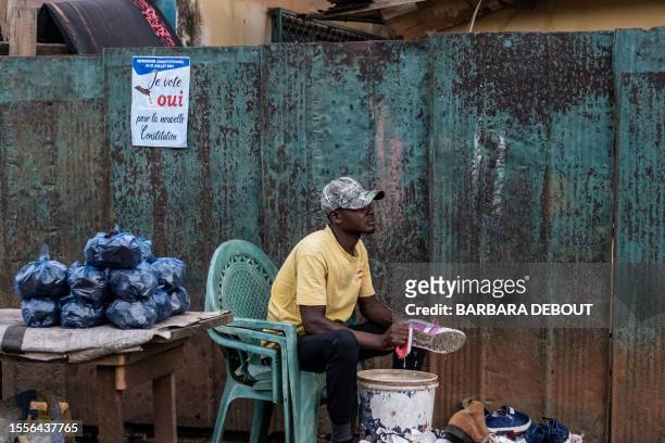 Small poster urging people to vote yes in the upcoming referendum is seen on the wall of a house behind a man cleaning shoes in Bangui, on July 25,...