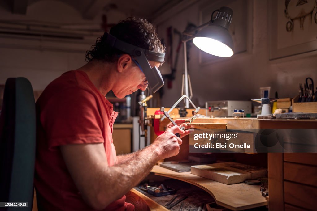 Portrait of a male Caucasian jeweller sawing metal in his workshop