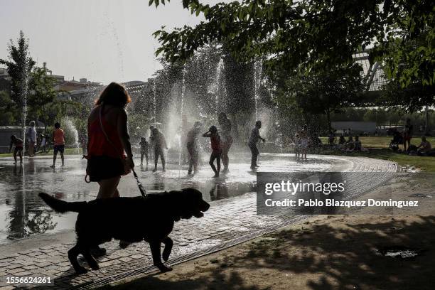 Woman walks a dog as children cool off and play at a fountain in Madrid Rio during the elections campaign as Spain faces another heatwave on July 19,...