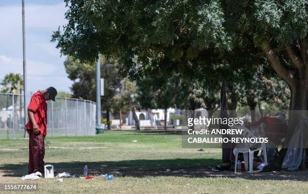 Homeless man stands in the shade of a tree near a bottle of water in Tucson, Arizona on July 26, 2023. A record-breaking heat wave stretching across...