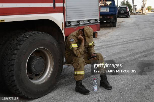 Firefighter looks at his mobile phoneas he rests during wildfires, near the industrial zone of the central Greek city of Volos on July 27, 2023....