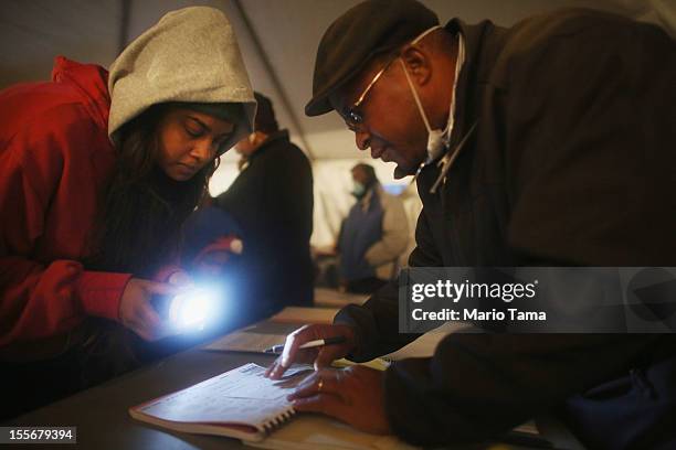 Rockaway resident Sheresa Walker uses a flashlight as poll worker Lloyd Edwards assists before voting in a makeshift tent set up as a polling place...