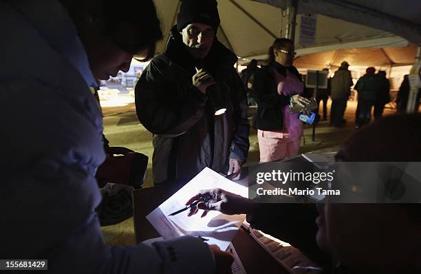 Poll worker assists voters with the help of a flashlight in a makeshift tent set up as a polling place at Scholars' Academy, PS 180, in the Rockaway...