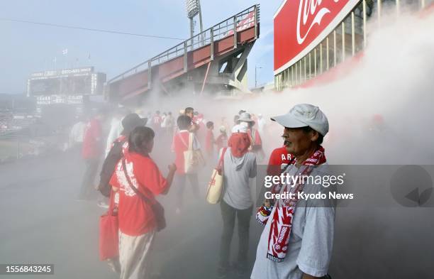 Baseball fans stand under mist showers on a sweltering hot day at Mazda Stadium in Hiroshima, western Japan, ahead of a game between the Hiroshima...