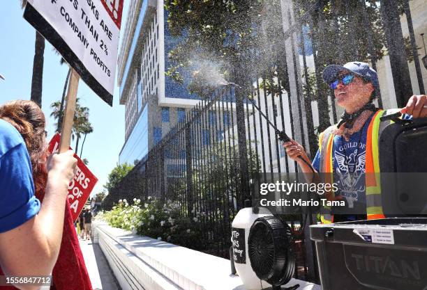 Strike captain Taylor Orci uses a mister and fan to cool off strikers in the summer heat as striking SAG-AFTRA and WGA members picket outside Netflix...