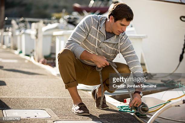 a man tying up a boat at the dock. - moored stock pictures, royalty-free photos & images