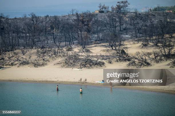 Woman enters the sea from a beach where wildfires destroyed the woods, at Glystra near the village of Gennadi in the southern part of the Greek...