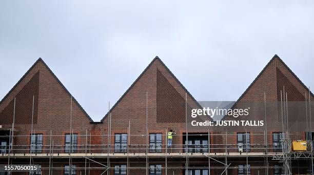 Worker stands on scaffolding to work outside a newly built residential property at a Barratt construction site for new houses and homes near...